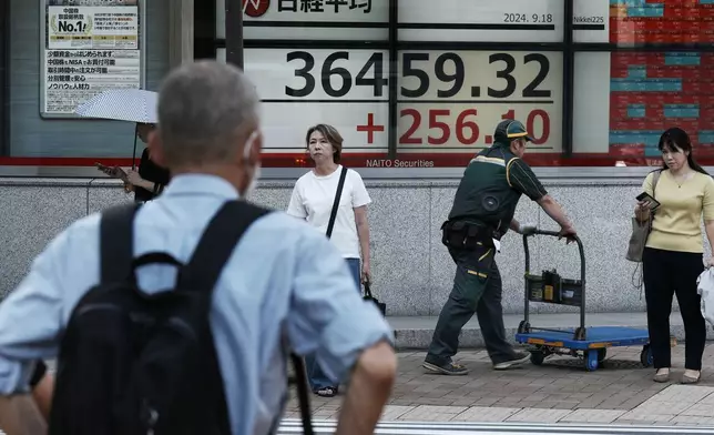 People stand near an electronic stock board showing Japan's Nikkei index at a securities firm Wednesday, Sept. 18, 2024, in Tokyo. (AP Photo/Eugene Hoshiko)