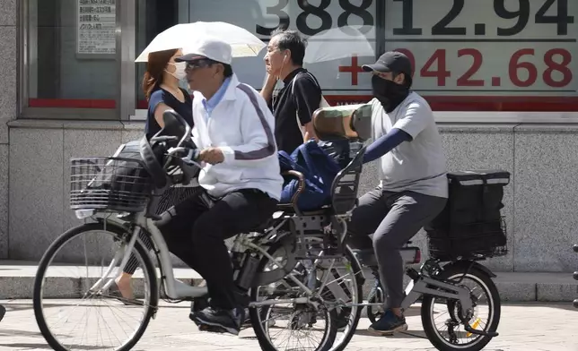 People ride bicycles in front of an electronic stock board showing Japan's Nikkei index at a securities firm Thursday, Sept. 26, 2024, in Tokyo. (AP Photo/Eugene Hoshiko)