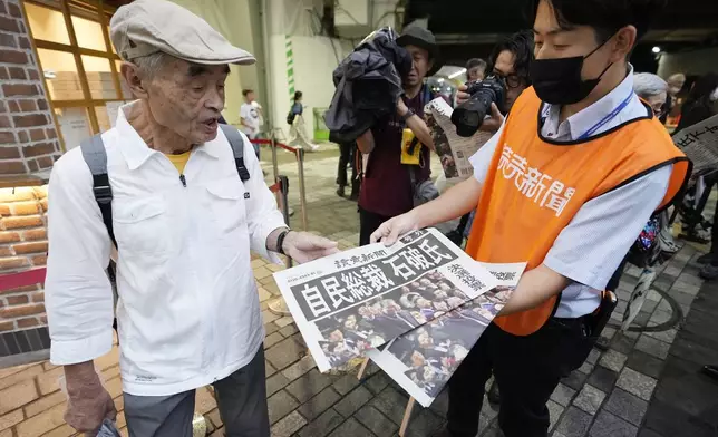 A pedestrian takes a copie of an extra edition of the Yomiuri newspaper reporting on Shigeru Ishiba becoming the winner of the Liberal Democratic Party's presidential election Friday, Sept. 27, 2024, in Tokyo. (AP Photo/Hiro Komae)