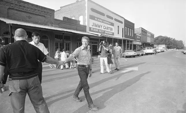 FILE - Democratic presidential nominee Jimmy Carter shakes hands with tourists as he takes an early morning walk down the main street of Plains, Ga., July 30, 1976. (AP Photo/Peter Bregg, File)