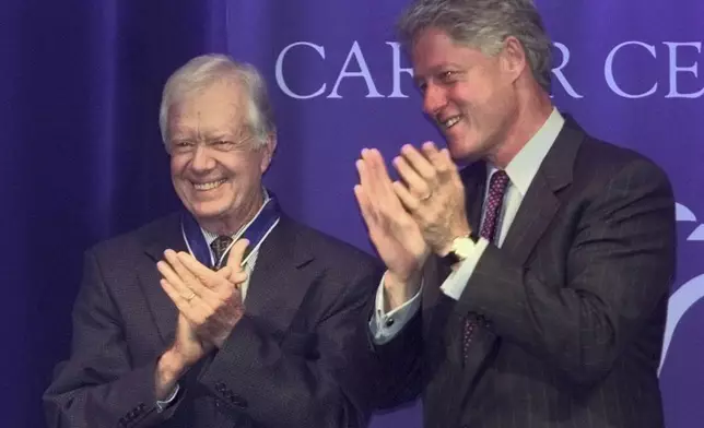 FILE - Former President Jimmy Carter and President Clinton applaud former first lady Rosalynn Carter as she speaks, after Clinton awarded the couple the Presidential Medal of Freedom, the nation's highest civilian honor, during a ceremony at the Carter Center in Atlanta, Aug. 9, 1999. (AP Photo/John Bazemore, File)