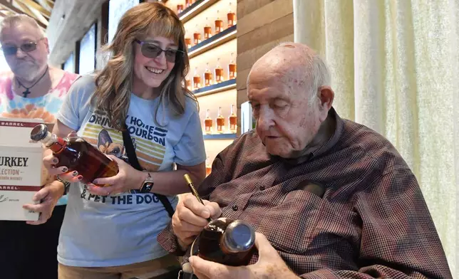 Donna Barton, left, of Princeton, W. Va., has 89-year-old Jimmy Russell, known as the "Buddha of Bourbon" sign a bottle of bourbon in the Visitors' Center at the Wild Turkey Distillery in Lawrenceburg, Ky., Wednesday, Aug. 28, 2024. (AP Photo/Timothy D. Easley)