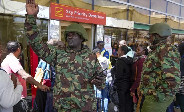 A Kenyan police officer gestures as stranded passengers wait for their delayed flights out of JKIA airport after flights were grounded following workers’ protesting a planned deal between the government and a foreign investor, in Nairobi, Kenya, Wednesday, Sept. 11, 2024. (AP Photo/Brian Inganga)