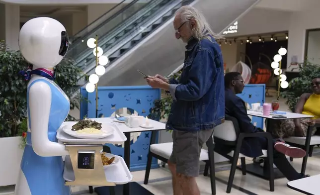 Robotic waiter Claire, delivers an order to customers at the Robot Cafe in Nairobi, Kenya Thursday, Aug. 29, 2024. The three robots, christened Claire, R24 and Nadia, are not programmed to have a full conversation with customers, but they can say "Your order is ready, Welcome" then people have to press an exit button after picking up their food from the tray. (AP Photo/Brian Inganga)