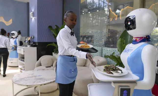 Robotic waiter Claire, receives an order from a human waiter to deliver to customers at the Robot Cafe in Nairobi, Kenya Thursday, Aug. 29, 2024. The three robots, christened Claire, R24 and Nadia, are not programmed to have a full conversation with customers, but they can say "Your order is ready, Welcome" then people have to press an exit button after picking up their food from the tray. (AP Photo/Brian Inganga)