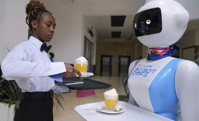 Robotic waiter Claire, receives an order from a human waiter to deliver to customers at the Robot Cafe in Nairobi, Kenya Thursday, Aug. 29, 2024. The three robots, christened Claire, R24 and Nadia, are not programmed to have a full conversation with customers, but they can say "Your order is ready, Welcome" then people have to press an exit button after picking up their food from the tray. (AP Photo/Brian Inganga)