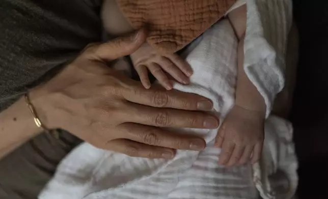 Robyn Joy Park, an adoptee from South Korea, gently pats her newborn daughter, Rae, at her home in Pasadena, Calif., Friday, April 19, 2024. (AP Photo/Jae C. Hong)