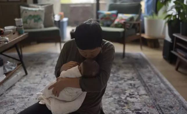 Robyn Joy Park, an adoptee from South Korea, kisses her newborn daughter, Rae, on the forehead at her home in Pasadena, Calif., Friday, April 19, 2024. (AP Photo/Jae C. Hong)