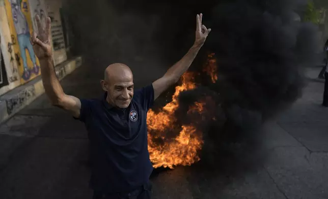 A retired member of the Lebanese security flashes victory sign next of tires that set on fire to block a road leading to the government palace, during a protest demanding an increase in their monthly retirement pay, decimated in the economic meltdown, in Beirut, Lebanon, Tuesday, Sept. 10, 2024. (AP Photo/Bilal Hussein)