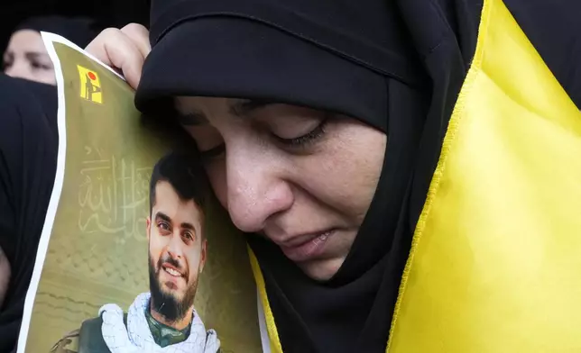 A woman holds a picture of a Hezbollah member who was killed on Wednesday when a handheld device exploded, during his funeral procession in the southern suburbs of Beirut, Thursday, Sept. 19, 2024. (AP Photo/Hussein Malla)