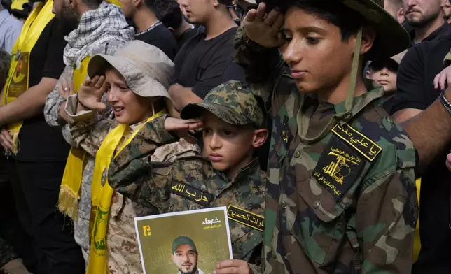 Boys salute during the funeral procession of Hezbollah members who were killed on Wednesday when a handheld device exploded, in the southern suburbs of Beirut, Thursday, Sept. 19, 2024. (AP Photo/Hussein Malla)