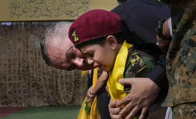 A man comforts a boy crying during the funeral procession of Hezbollah members in the southern suburbs of Beirut, Thursday, Sept. 19, 2024. (AP Photo/Hussein Malla)