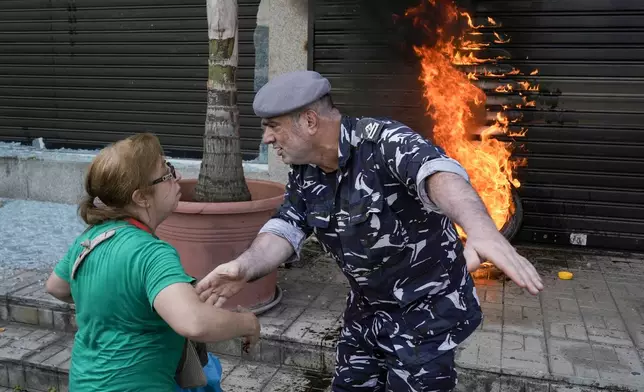 FILE - A police officer speaks with a protesting depositor as they stand in front of burning tires set on fire in front of a branch of Emirates Lebanese Bank in Dawra, a suburb north-east of Beirut, on Aug. 29, 2024. (AP Photo/Bilal Hussein, File)