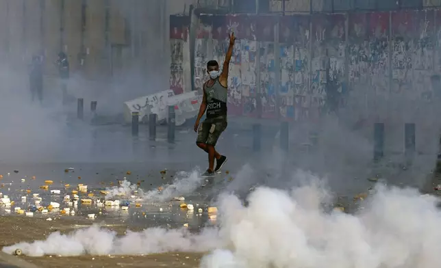 FILE - An anti-government protester flashes the victory sign amid tear gas fired by riot police during a protest marking the first anniversary of the massive blast at Beirut's port, near Parliament Square, in Beirut, on Aug. 4, 2021. (AP Photo/Bilal Hussein, File)