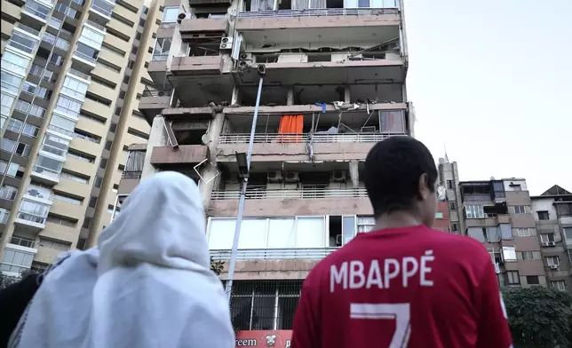 People look up at a damaged building that was hit by Israeli strike early Monday, Sept. 30, 2024, in Beirut, Lebanon. (AP Photo/Hussein Malla)