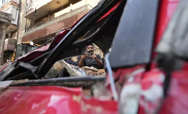 A man uses his mobile phone to document a damaged car at the scene of the building that was hit by an Israeli airstrike in Beirut's southern suburbs, Tuesday, Sept. 24, 2024. (AP Photo/Hassan Ammar)