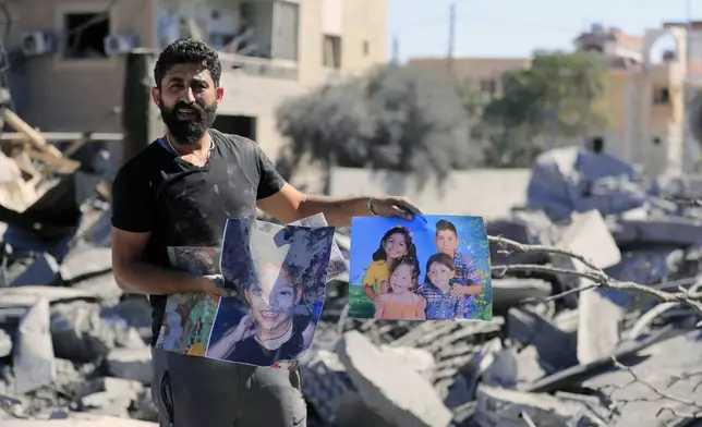 A man carries pictures of his relatives standing at the site of an Israeli airstrike in Saksakieh, south Lebanon, Thursday, Sept. 26, 2024. (AP Photo/Mohammed Zaatari)