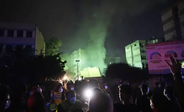 People gather as smoke rises from a collapsed building at the site of an Israeli airstrike in Beirut's southern suburbs, Friday, Sept. 27, 2024. (AP Photo/Hassan Ammar)