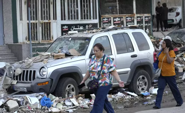 Women pass the damaged cars where an Israeli airstrike hit a building in Beirut early Monday, Sept. 30, 2024. (AP Photo/Hussein Malla)