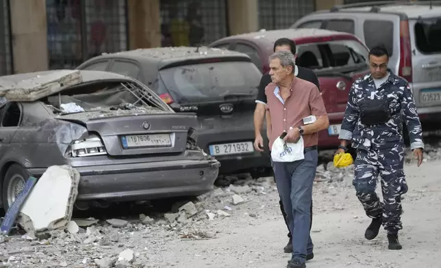 People walk past damaged cars near a building hit by an Israeli airstrike early Monday, Sept. 30, 2024, in Beirut, Lebanon. (AP Photo/Hussein Malla)