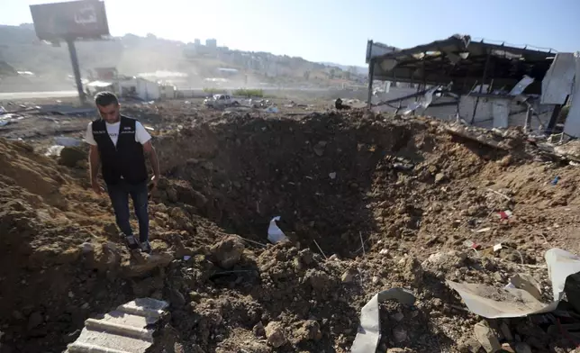 A Lebanese police intelligence stands near a crater at the site of an Israeli airstrike that hit a hangar in the southern town of Jiyeh, Lebanon, Wednesday, Sept. 25, 2024. (AP Photo/Mohammed Zaatari)