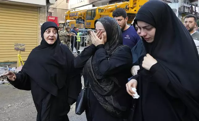 Residents cry as they walk past a building that was hit by an Israeli airstrike in Beirut's southern suburbs, Tuesday, Sept. 24, 2024. (AP Photo/Hassan Ammar)