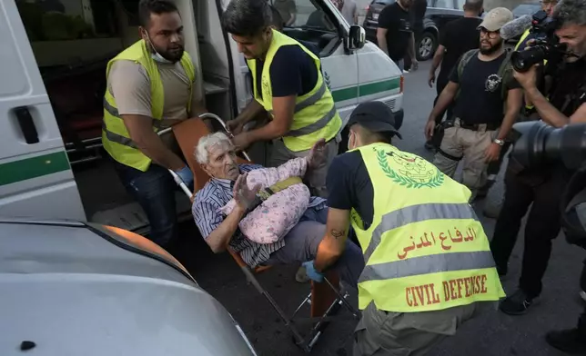 Civil defense workers carry an elderly, fleeing the south, as he arrives at a school turned into a shelter in Beirut, Monday, Sept. 23, 2024. (AP Photo/Bilal Hussein)