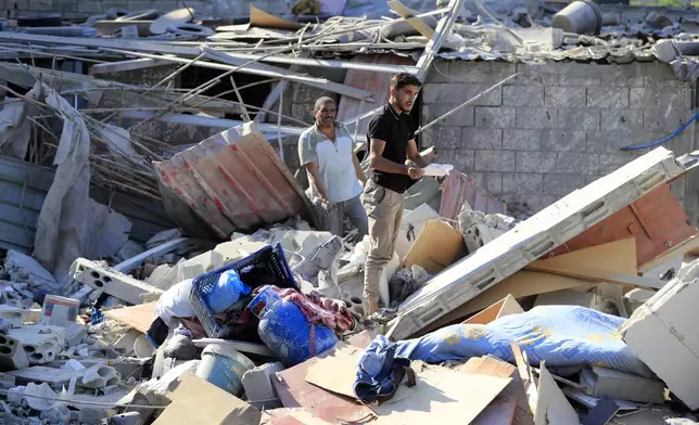 Men stand on the rubble of a building hit in an Israeli airstrike in the southern village of Akbieh, Lebanon, Tuesday, Sept. 24, 2024. (AP Photo/Mohammed Zaatari)