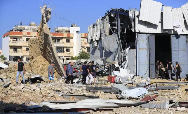 People gather at the site of an Israeli airstrike that hit a hangar in the southern town of Jiyeh, Lebanon, Wednesday, Sept. 25, 2024. (AP Photo/Mohammed Zaatari)