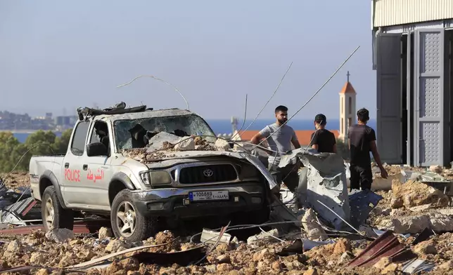 People gather near a damaged car at the site of an Israeli airstrike that hit a hangar in the southern town of Jiyeh, Lebanon, Wednesday, Sept. 25, 2024. (AP Photo/Mohammed Zaatari)