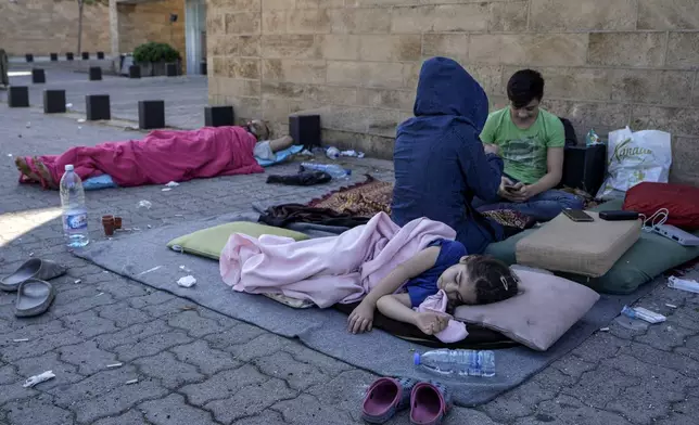 A family sleep on the ground in Beirut's corniche area after fleeing the Israeli airstrikes in the southern suburbs of Dahiyeh, Sunday, Sept. 29, 2024. (AP Photo/Bilal Hussein)