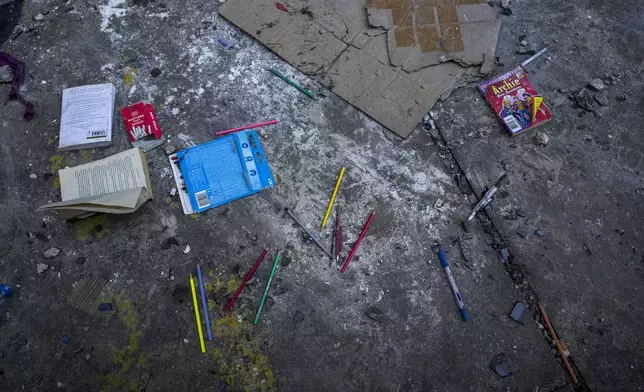 Coloring pencils and books are scattered on the ground outside a building that was hit by an Israeli airstrike in Beirut's southern suburbs, Thursday, Sept. 26, 2024. (AP Photo/Hassan Ammar)