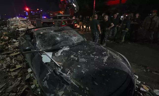 Policemen and civil defense workers stand next to damaged cars near a building that was hit in an Israeli airstrike, in Beirut, Lebanon, early Monday, Sept. 30, 2024. (AP Photo/Bilal Hussein)