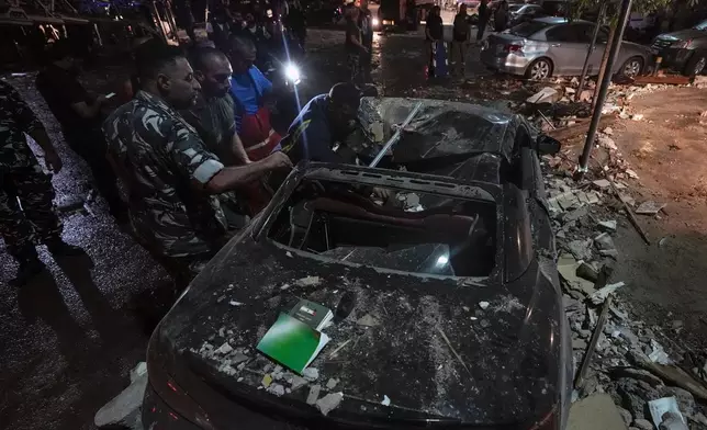 Policemen and civil defense workers inspect a damaged car near a building that was hit in an Israeli airstrike, in Beirut, Lebanon, early Monday, Sept. 30, 2024. (AP Photo/Bilal Hussein)