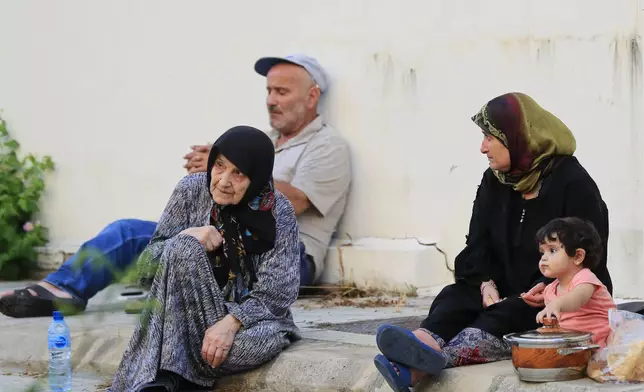 People fleeing the southern villages amid ongoing Israeli airstrikes, sit on the sidewalk outside a school in Sidon, Monday, Sept. 23, 2024. (AP Photo/Mohammed Zaatari)