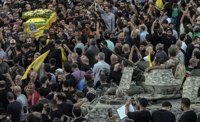 Lebanese army soldiers sit on their armoured vehicle as mourners carry the coffin of Mohammed Mahdi, son of Hezbollah legislator Ali Ammar, who was killed Tuesday after his handheld pager exploded, in the southern suburb of Beirut, Lebanon, Wednesday, Sept. 18, 2024. (AP Photo/Bilal Hussein)