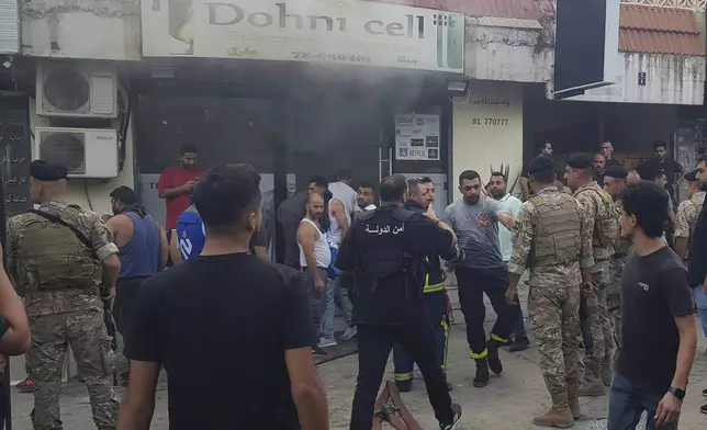 Lebanese soldiers and firefighters gather outside a mobile shop after what is believed to be the result of a walkie-talkie exploding inside it, in the southern port city of Sidon, Lebanon, Wednesday, Sept. 18, 2024. (AP Photo/Mohammed Zaatari)