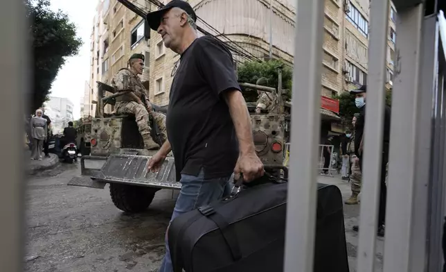 A man walks with a suitcase as Lebanese soldiers drive near the site of Friday's Israeli strike in Beirut's southern suburb, Sunday, Sept. 22, 2024. (AP Photo/Bilal Hussein)