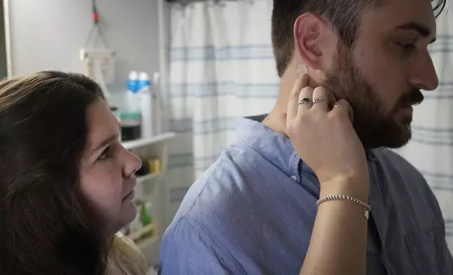 Julia Manetta applies an anti-nausea patch on the neck of her husband, Steven, a cancer patient, Thursday, Aug. 29, 2024, in their Lemont, Ill., home. (AP Photo/Charles Rex Arbogast)