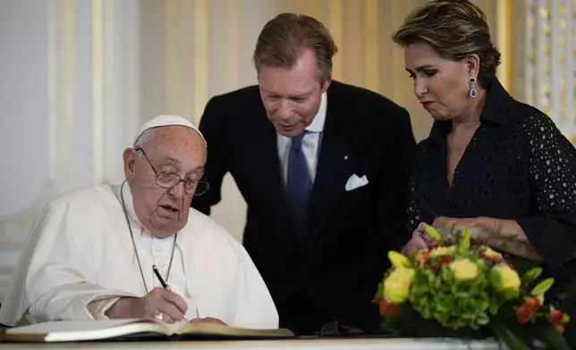 Pope Francis flanked by Luxembourg's Grand Duke Henri and Grand Duchess Maria Teresa signs the guest book during his visit at the Grand Ducal Palace, in Luxembourg, Thursday, Sept. 26, 2024. (AP Photo/Andrew Medichini)