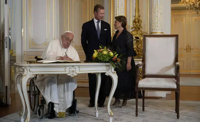 Pope Francis flanked by Luxembourg's Grand Duke Henri and Grand Duchess Maria Teresa signs the guest book during his visit at the Grand Ducal Palace, in Luxembourg, Thursday, Sept. 26, 2024. (AP Photo/Andrew Medichini)