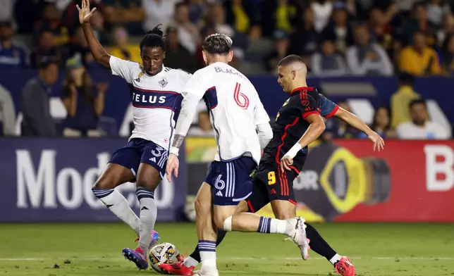 Los Angeles Galaxy's Dejan Joveljic, right, vies for the ball against Vancouver Whitecaps' Sam Adekugbe, left, and Tristan Blackmon during the second half of an MLS soccer match Saturday, Sept. 21, 2024, in Carson, Calif. (AP Photo/Etienne Laurent)