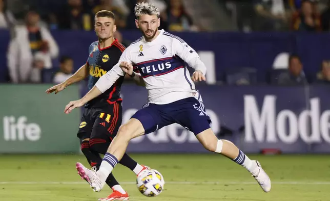 Los Angeles Galaxy's Gabriel Pec, left, shoots past Vancouver Whitecaps' Tristan Blackmon during the second half of an MLS soccer match Saturday, Sept. 21, 2024, in Carson, Calif. (AP Photo/Etienne Laurent)