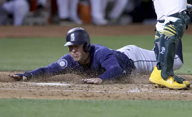 Seattle Mariners shortstop Dylan Moore (25) slides to home plate, safe on a single hit by Julio Rodríguez during the seventh inning of a baseball game against the Oakland Athletics in Oakland, Calif., Wednesday, Sept. 4, 2024. (AP Photo/Jed Jacobsohn)