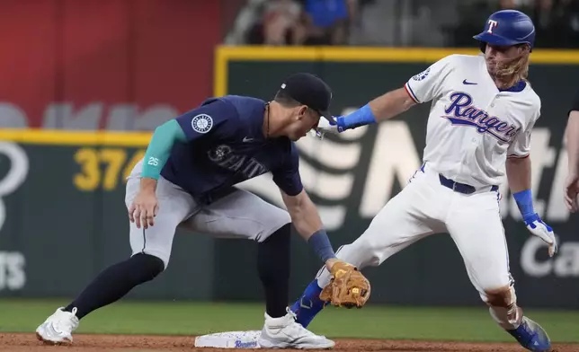 Texas Rangers' Travis Jankowski, right, reaches base against a tag by Seattle Mariners shortstop Dylan Moore, left, for a double hit during the second inning of a baseball game Saturday, Sept. 21, 2024, in Arlington, Texas. (AP Photo/LM Otero)