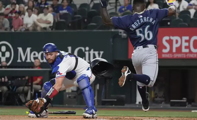 Seattle Mariners' Randy Arozarena (56) leaps scoring against Texas Rangers catcher Carson Kelly (18) on a single hit by Mariners Jorge Polanco during the first inning of a baseball game Saturday, Sept. 21, 2024, in Arlington, Texas. (AP Photo/LM Otero)