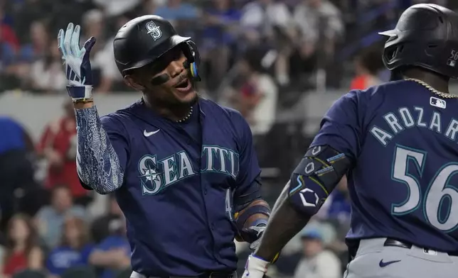 Seattle Mariners' Julio Rodríguez, left, celebrates after his home run with teammate Randy Arozarena (56) during the first inning of a baseball game against the Texas Rangers, Saturday, Sept. 21, 2024, in Arlington, Texas. (AP Photo/LM Otero)