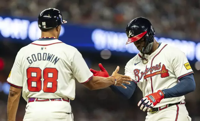 Atlanta Braves' Jorge Soler, right, high fives first base coach Tom Goodwin, left, after hitting a single in the fifth inning of a baseball game against the New York Mets, Tuesday, Sept. 24, 2024, in Atlanta. (AP Photo/Jason Allen)