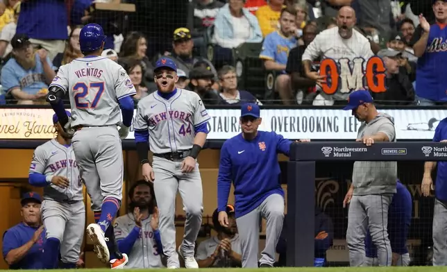 New York Mets' Mark Vientos (27) is congratulated at the dugout by Harrison Bader (44) after hitting a two-run home run during the third inning of a baseball game against the Milwaukee Brewers, Friday, Sept. 27, 2024, in Milwaukee. (AP Photo/Aaron Gash)