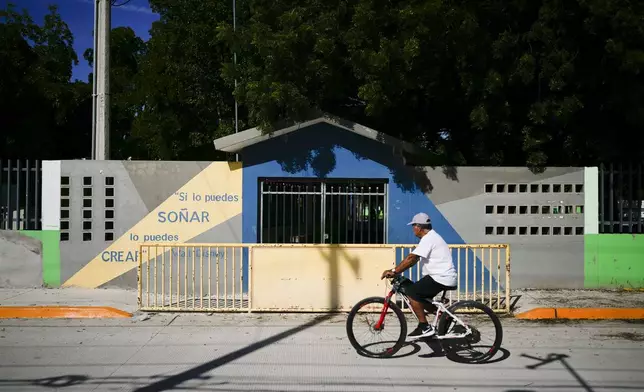 A resident pedals his bicycle past the temporarily closed Lazaro Cardenas elementary school, in Culiacan, Sinaloa state, Mexico, Thursday, Sept. 19, 2024. (AP Photo/Eduardo Verdugo)